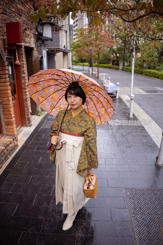 穿着和服/袴的年轻女子在下雨天走在城里-看着相机